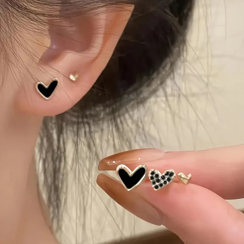 Three pairs of heart-shaped alloy earrings in gold, black, black and white, and pink colours with electroplated finish