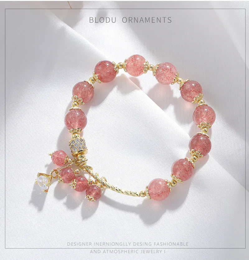 Close-up of a women's pink strawberry quartz heart bracelet with pearl details on a wrist.