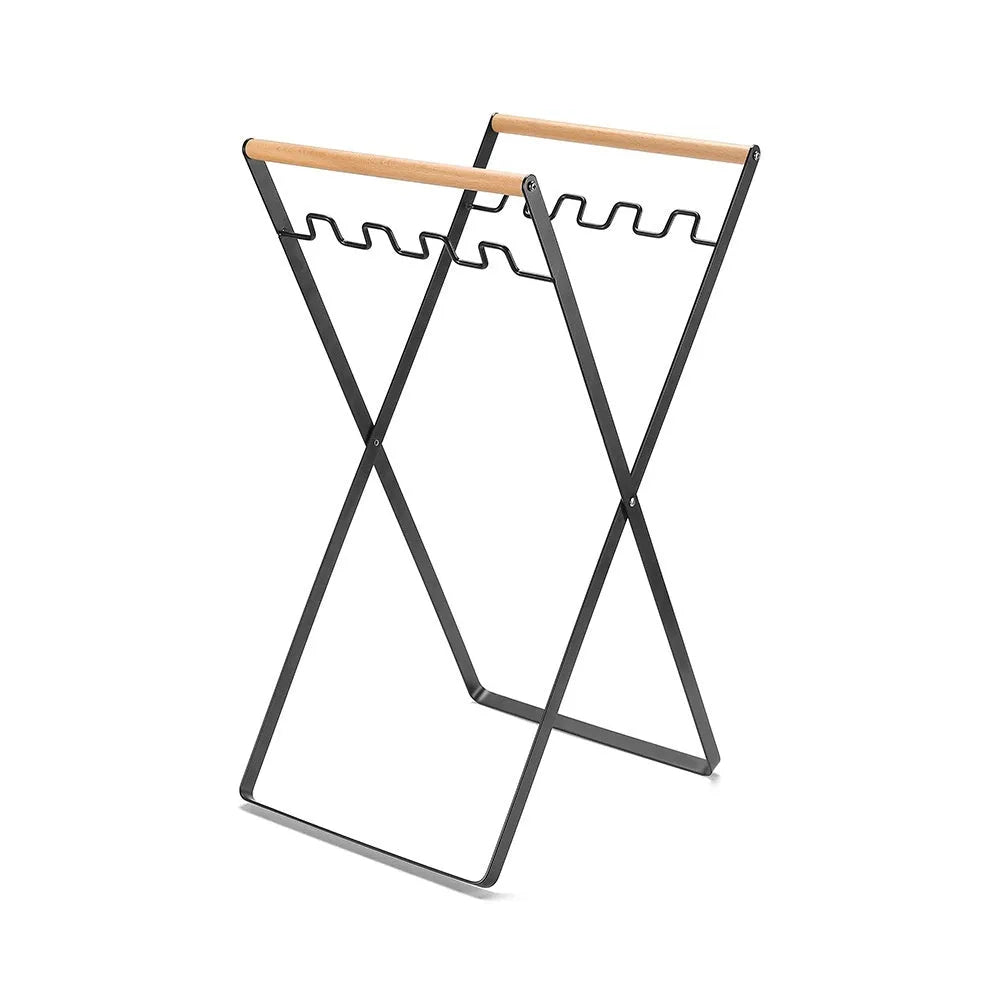 Black iron folding trash rack with wooden handle holding a bin bag outdoors.
