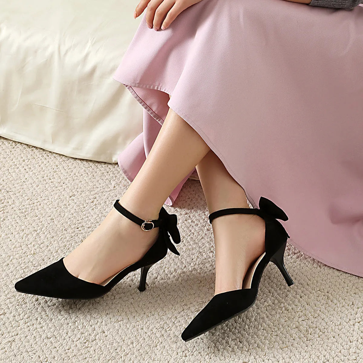 Black suede pointed-toe stiletto high heels with a bowknot detail and buckle ankle strap.