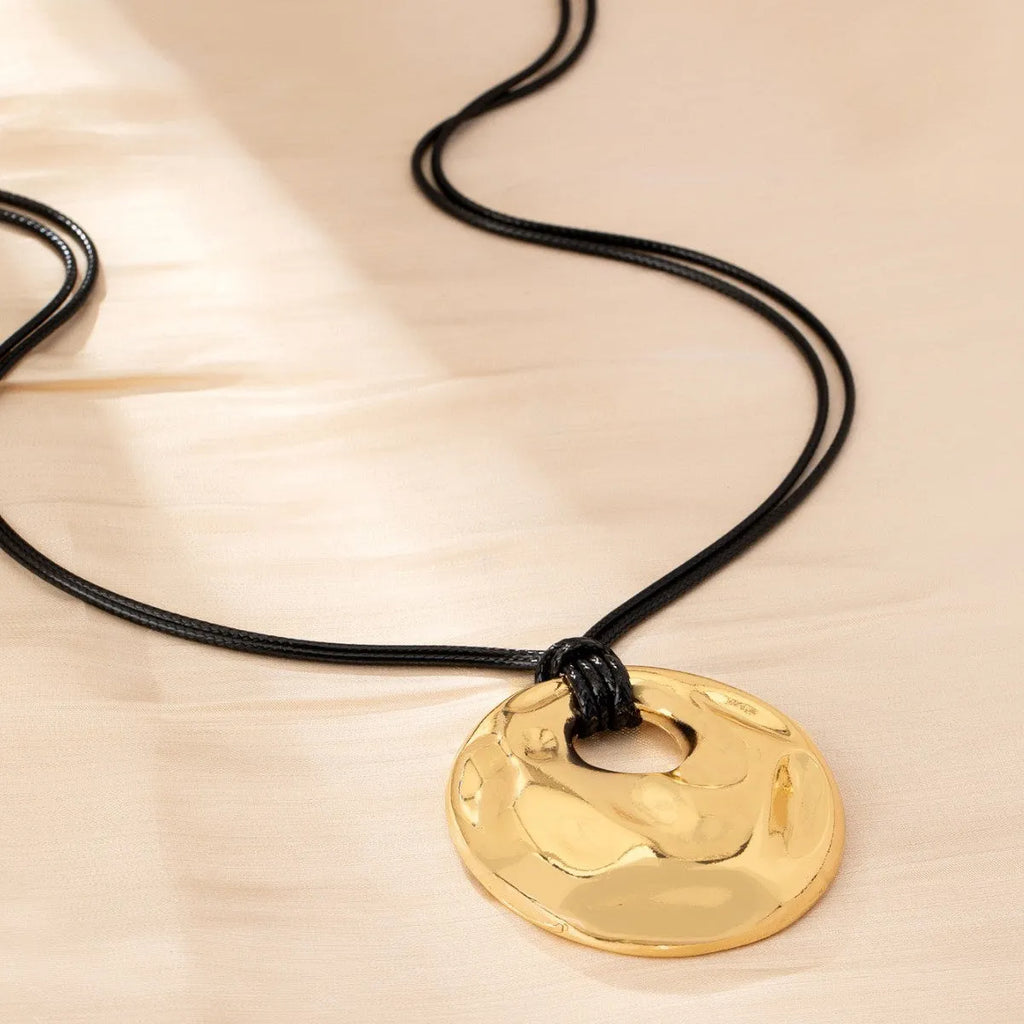 Women's gold alloy oval pendant necklace with braided rope chain on a plain background