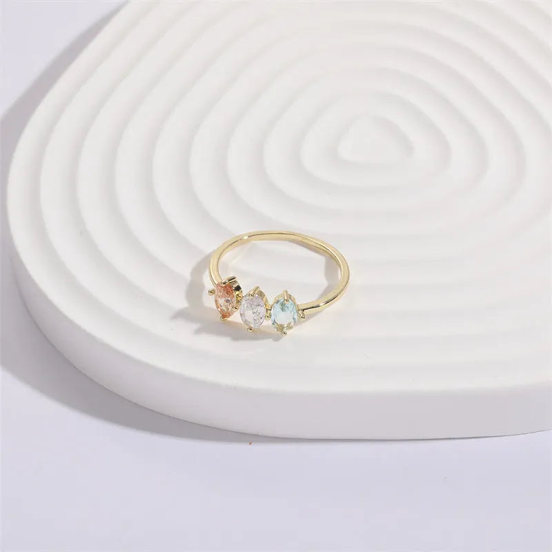 Gold colour geometric triangle ring with horse eye design and tricolour zircon stones on a white background