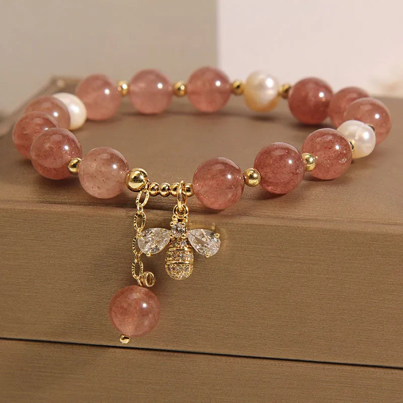 Women's pink strawberry quartz and white freshwater pearl bracelet with zircon details on wrist.