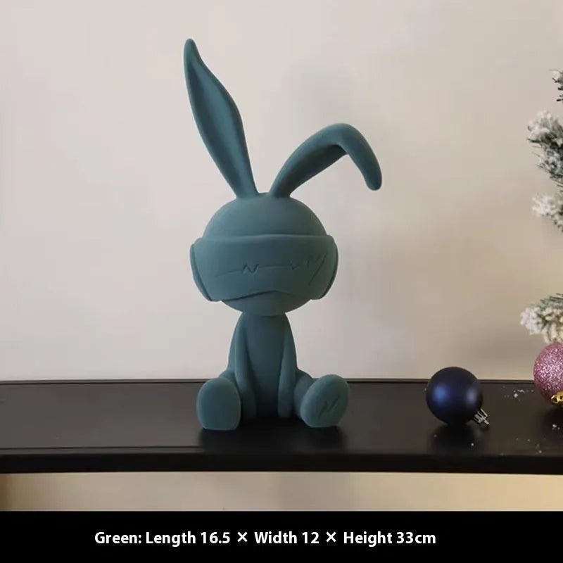 Small resin rabbit ornament wearing a suede blindfold, shown in blue, green, and red colour options.