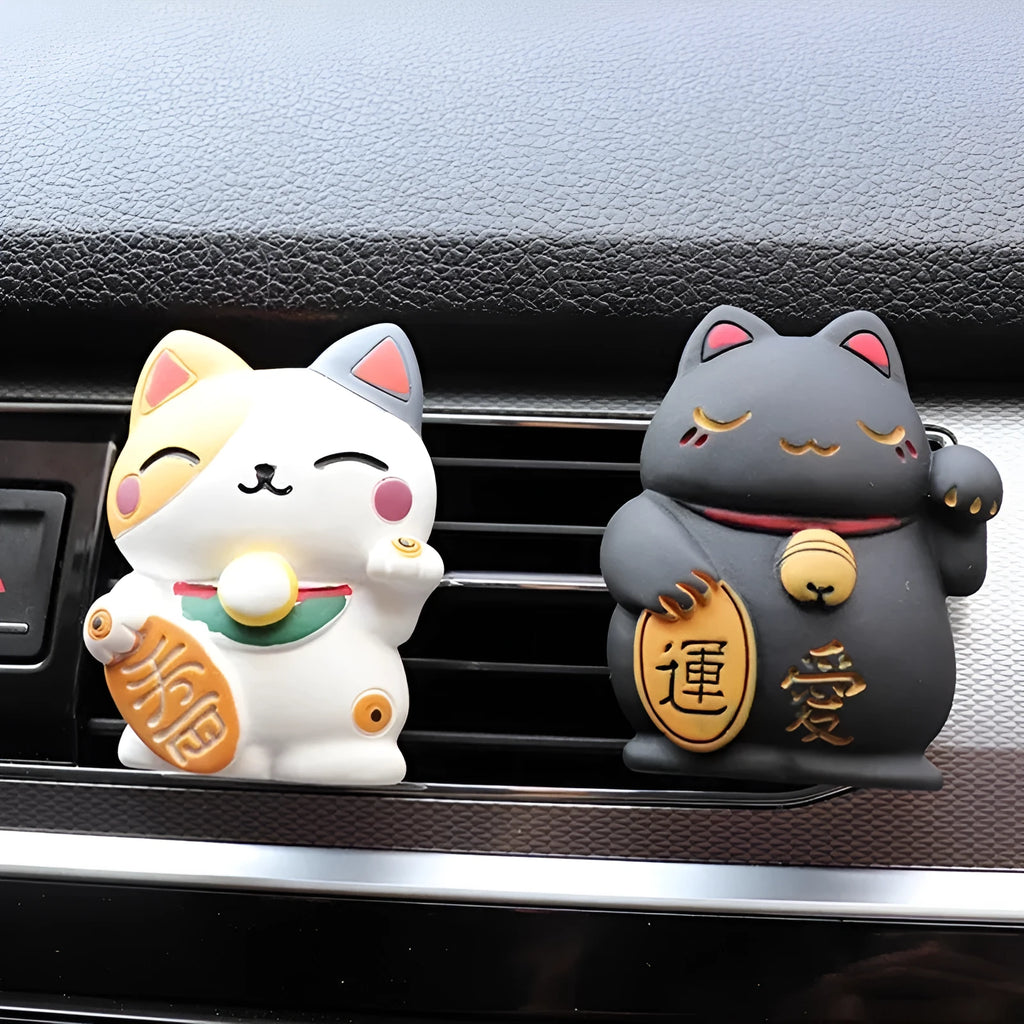 Black and white resin fortune cat ornament designed to clip onto a car air vent as an aromatherapy diffuser.