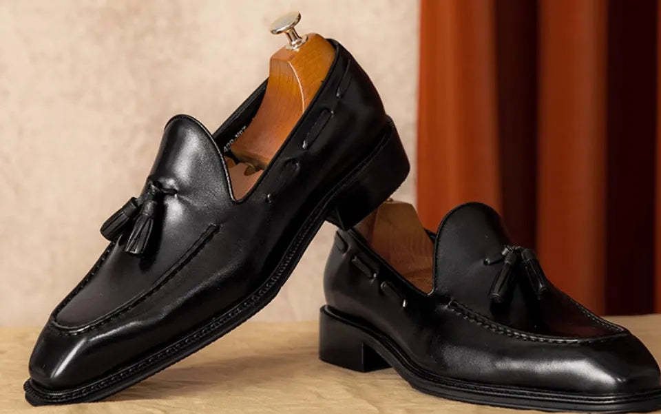 Men's black genuine leather slip-on loafers with a fringed design and rubber sole.