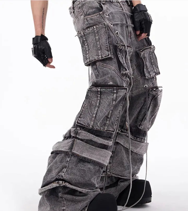 A pair of grey distressed denim overalls with rope stitching, shown on a model.