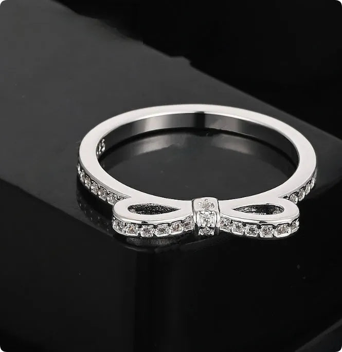 Silver bow-shaped ring with sparkling zircon crystal stones on a finger.