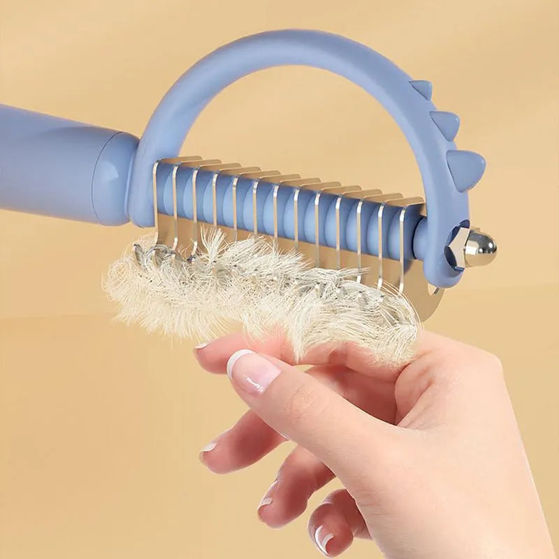 Blue dinosaur-shaped self-cleaning cat brush with double-sided stainless steel pins.