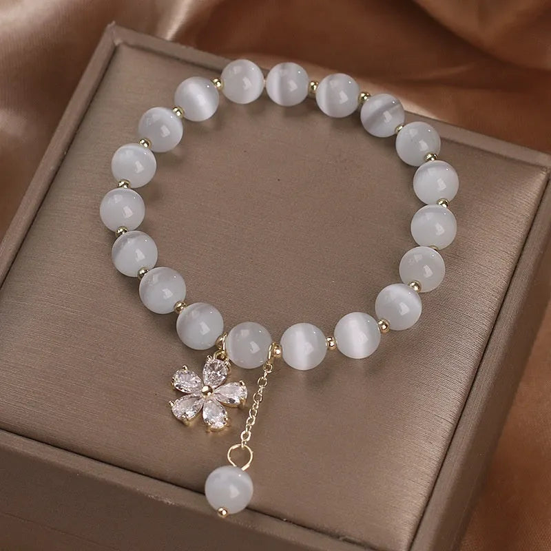 White cat's eye crystal women's bracelet with safety buckle pendant and small flower tassel on a single loop.