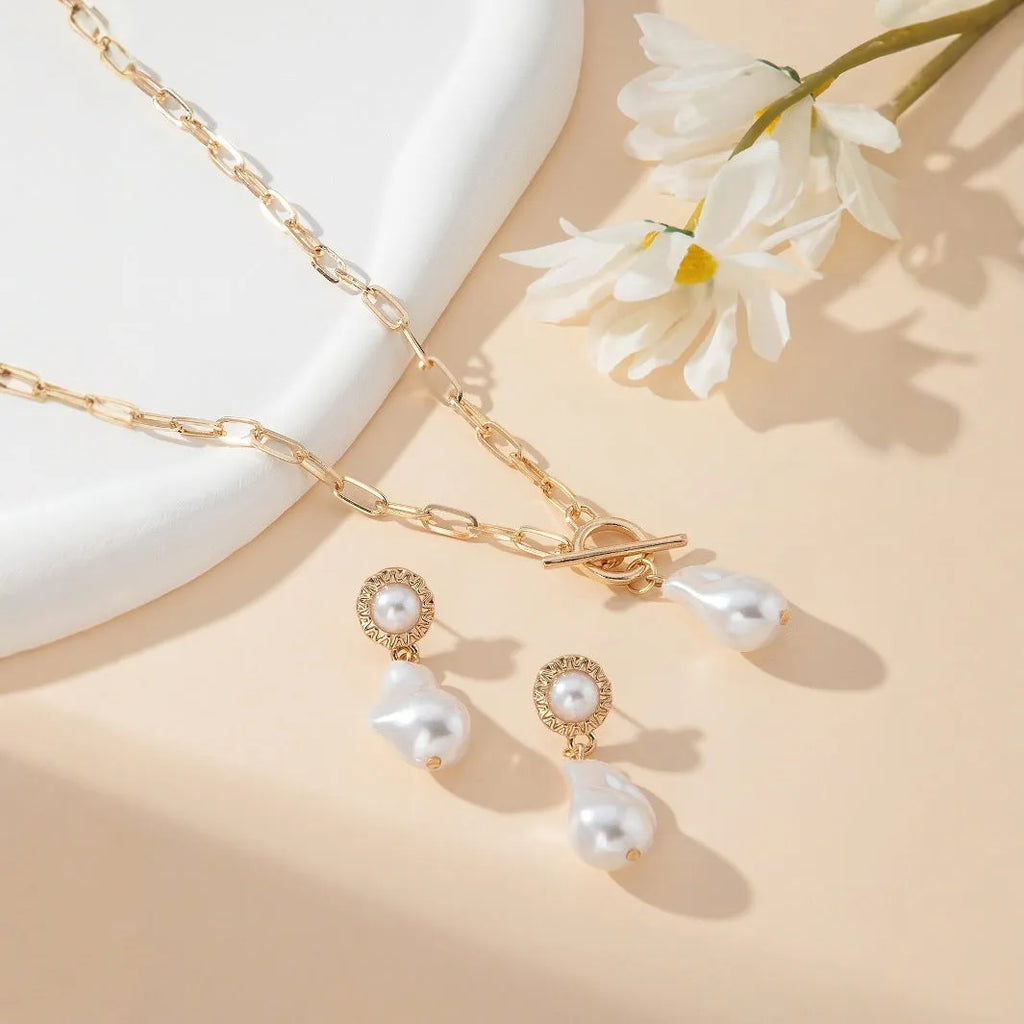 Gold-colour iron necklace and earring set with a baroque pearl pendant on a woman.