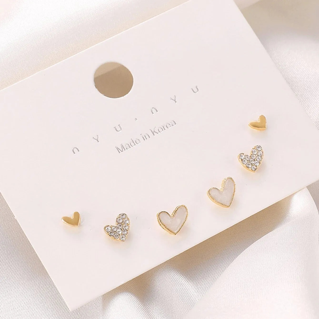 Three pairs of heart-shaped alloy earrings in gold, black, black and white, and pink colours with electroplated finish
