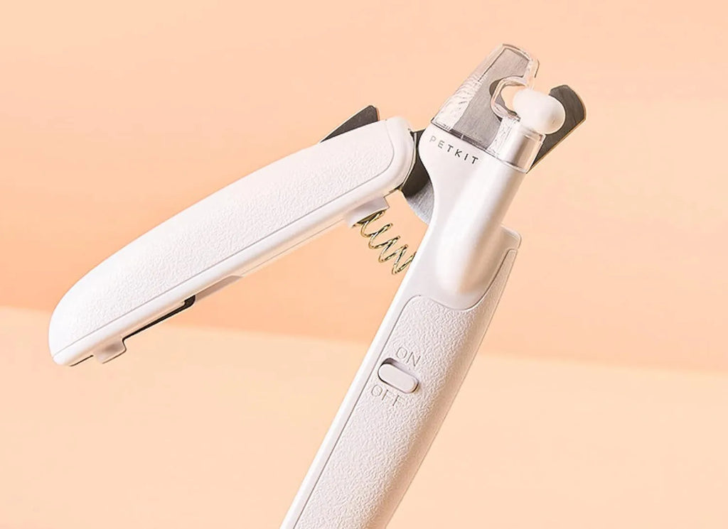 White pet nail clippers with LED light, transparent guard, and a nail file on a table