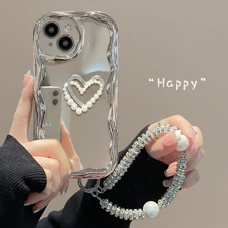 Silver grey silicone phone case for iPhone 15 Pro Max with three-dimensional pearls and chain, electroplated finish, and matching bracelet on a table