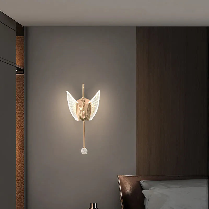 Gold swan-shaped modern minimalist wall lamp with acrylic shade on a wall.