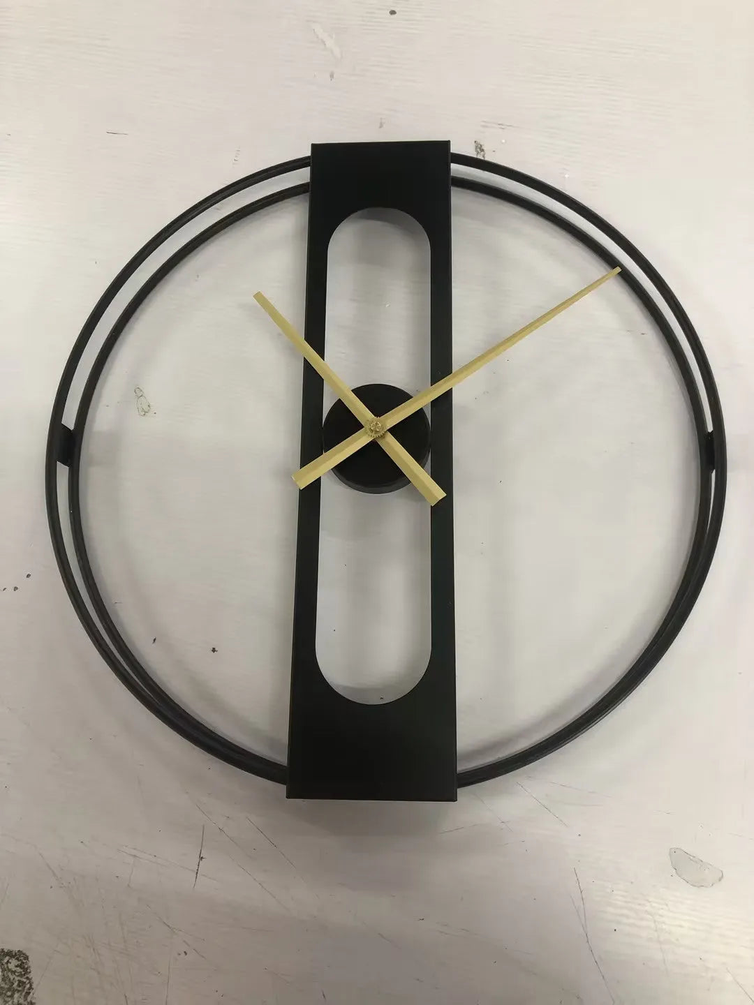 Large round metal wall clock with black dial and gold Arabic numerals on a white wall