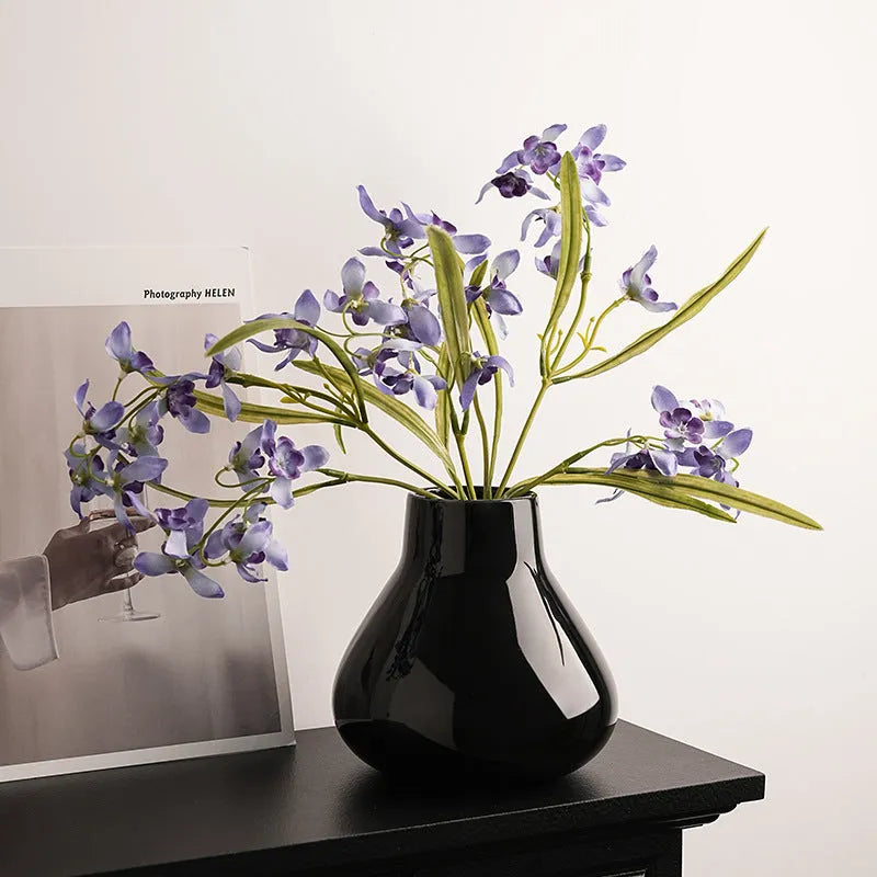 Black ceramic vase with round belly shape and two white flower ornaments arranged decoratively
