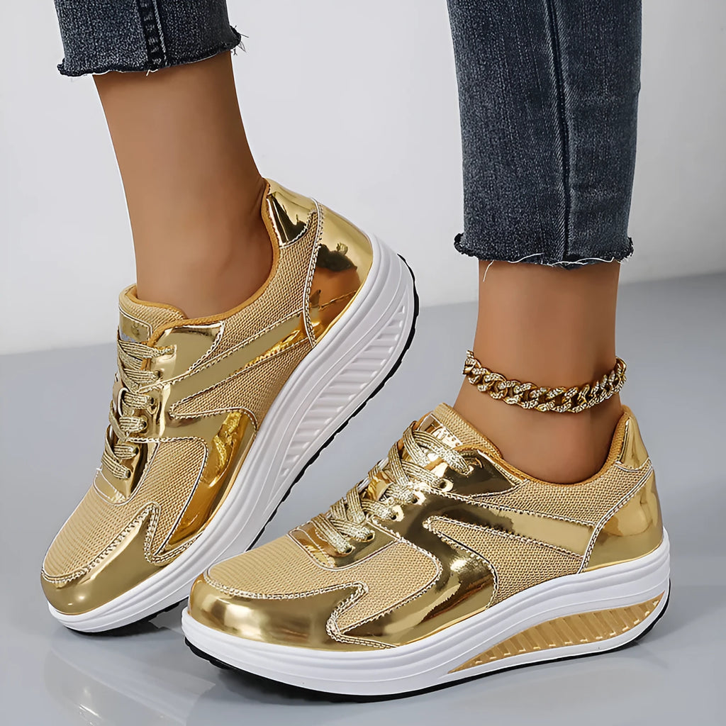 Gold women's mesh platform trainers with cross strap and thick sole on a white background.