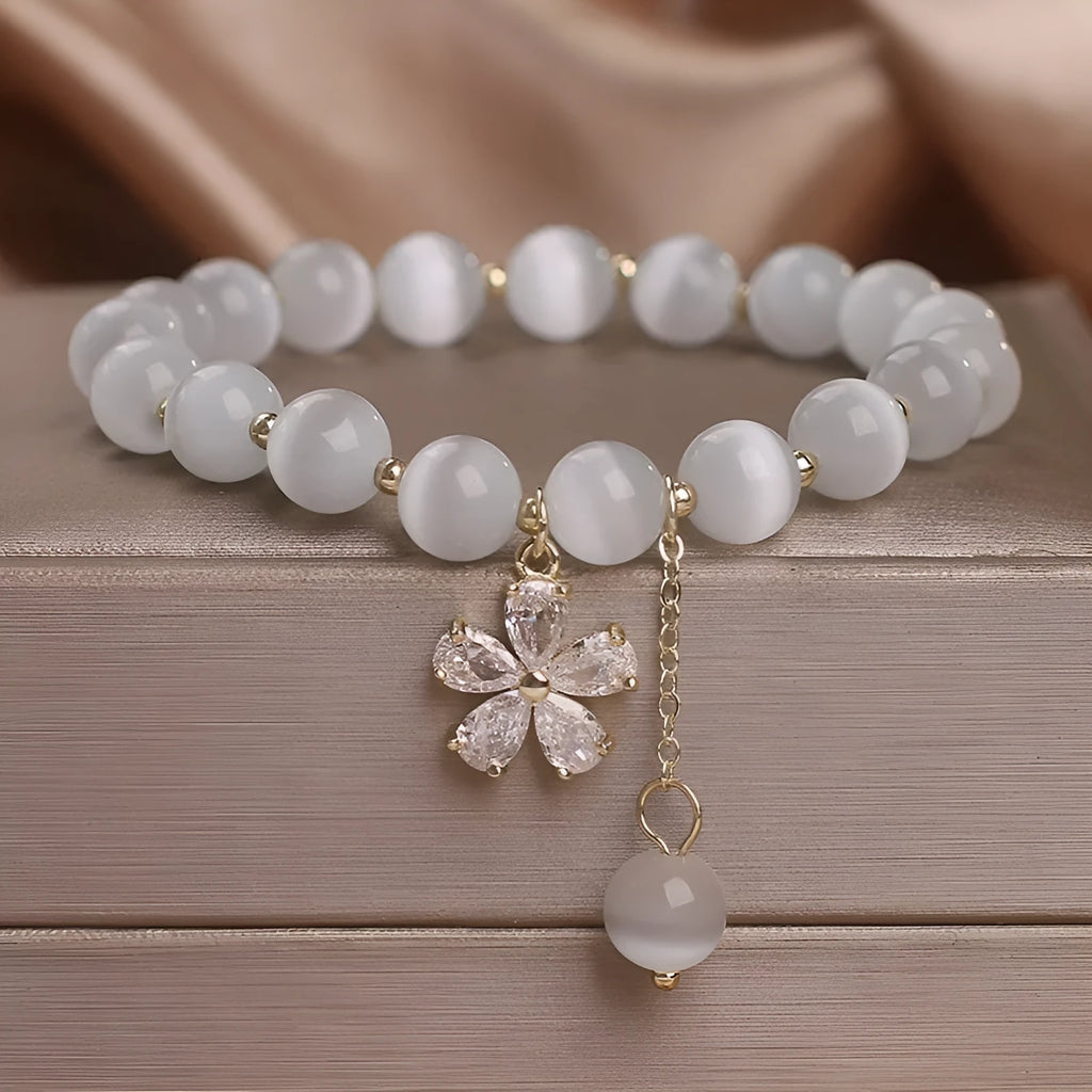 White cat's eye crystal women's bracelet with safety buckle pendant and small flower tassel on a single loop.