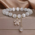 White cat's eye crystal women's bracelet with safety buckle pendant and small flower tassel on a single loop.