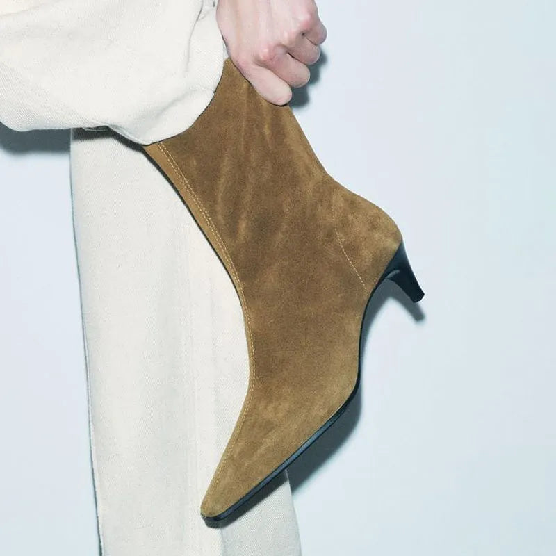 Brown square toe ankle boots with a side zipper and pointed stiletto heel on a wooden floor.