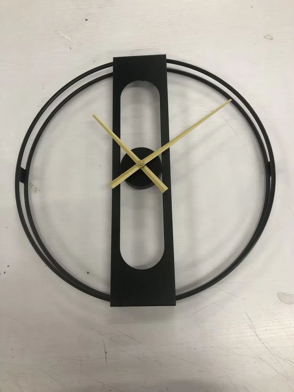 Large round metal wall clock with black dial and gold Arabic numerals on a white wall