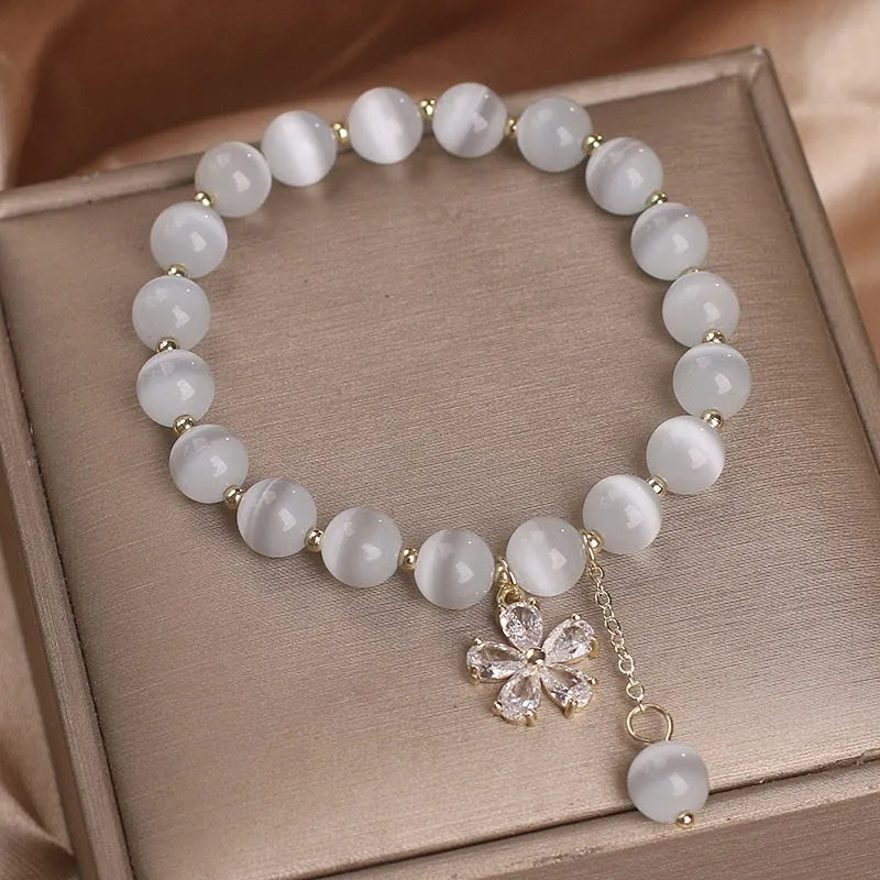 White cat's eye crystal women's bracelet with safety buckle pendant and small flower tassel on a single loop.