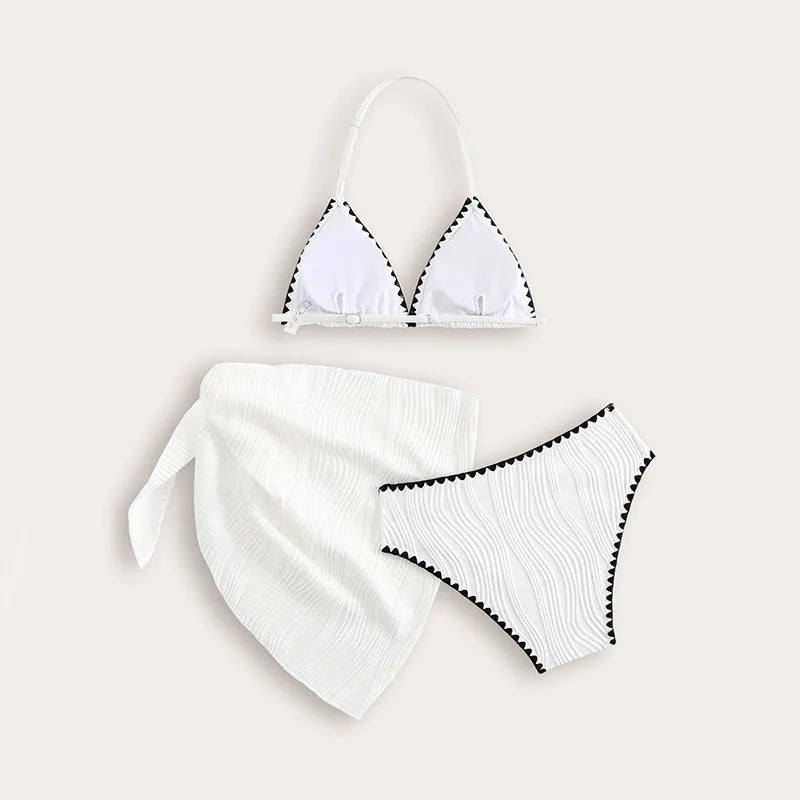 Solid white three-piece girls swimsuit set with top, pants, and skirt on a beach setting.
