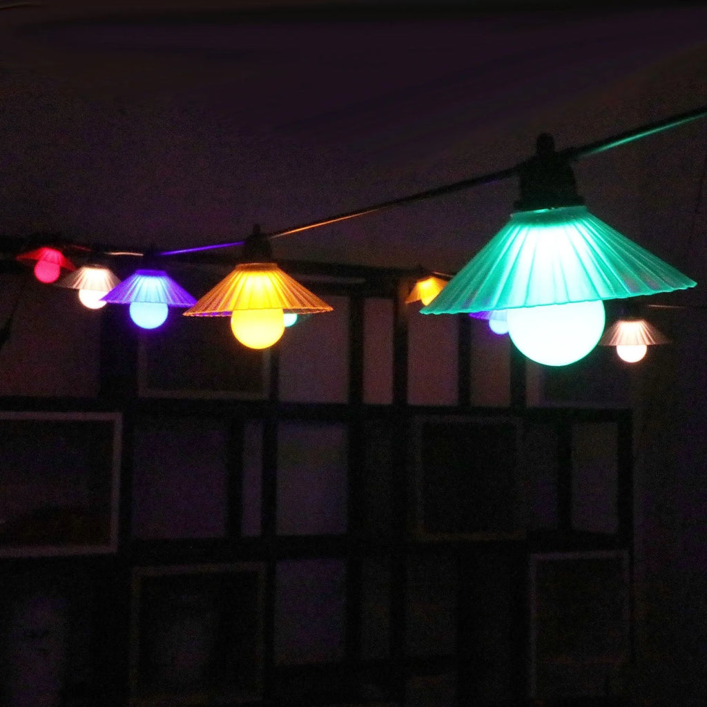 Outdoor LED string lights with white flower-shaped bulbs hanging in a garden.