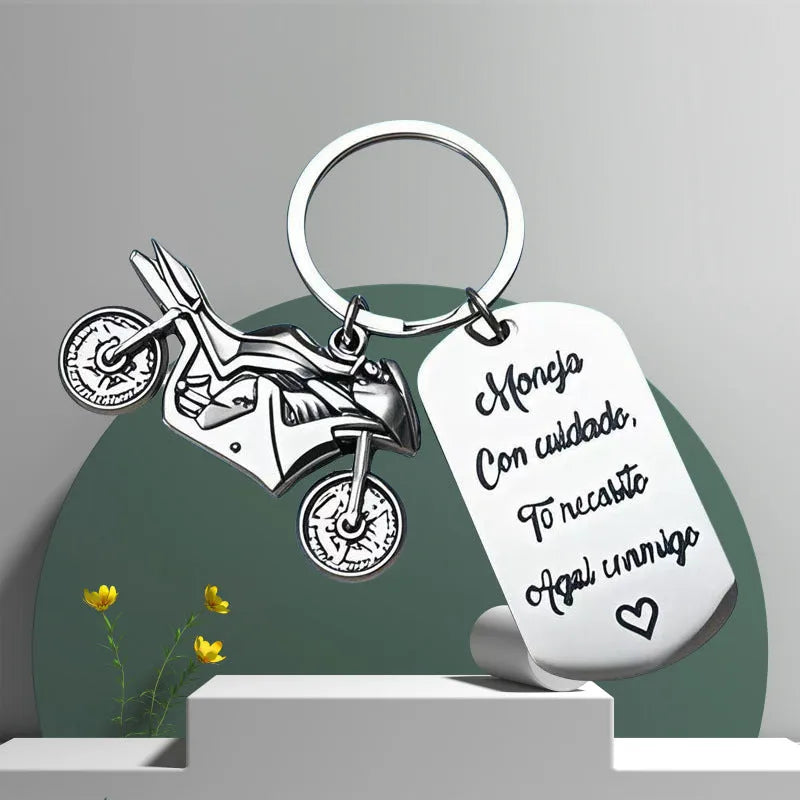 Stainless steel motorcycle key ring with velvet storage bag on a plain background.