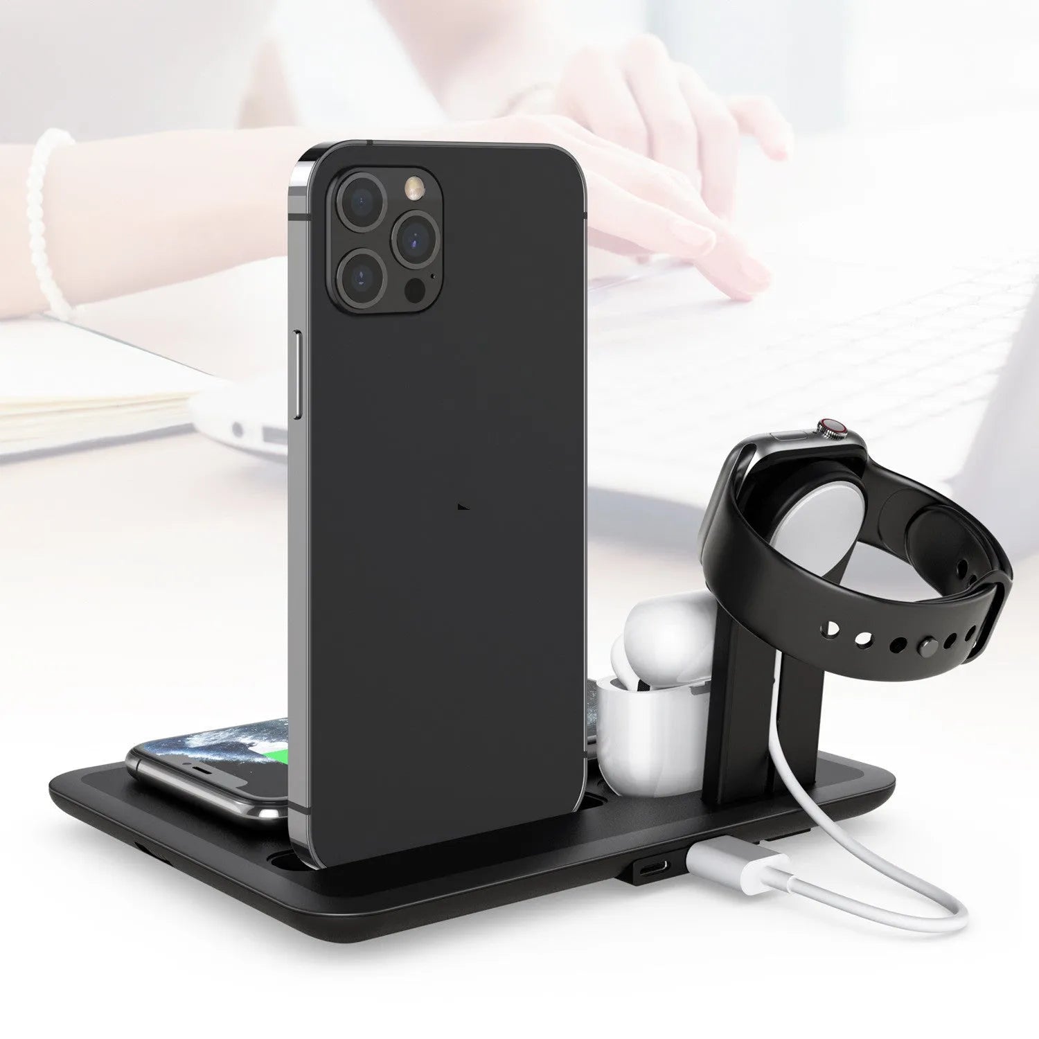 Black and white wireless charging station for mobile phone, smartwatch, and headphones on a desk.