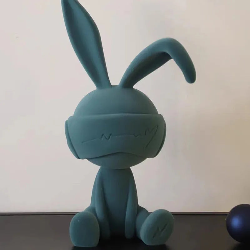 Small resin rabbit ornament wearing a suede blindfold, shown in blue, green, and red colour options.