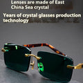 Dark green frameless crystal sunglasses with a matching case and cleaning cloth on a table.