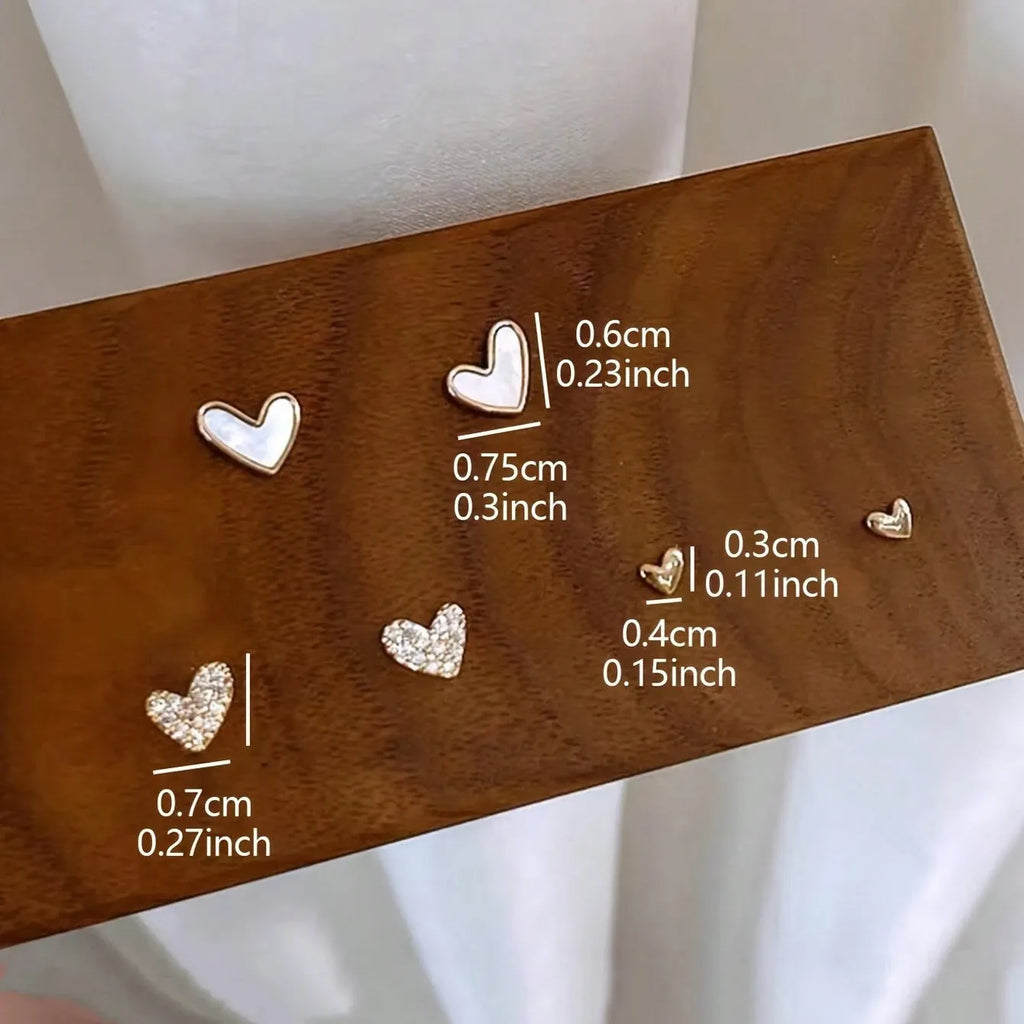 Three pairs of heart-shaped alloy earrings in gold, black, black and white, and pink colours with electroplated finish
