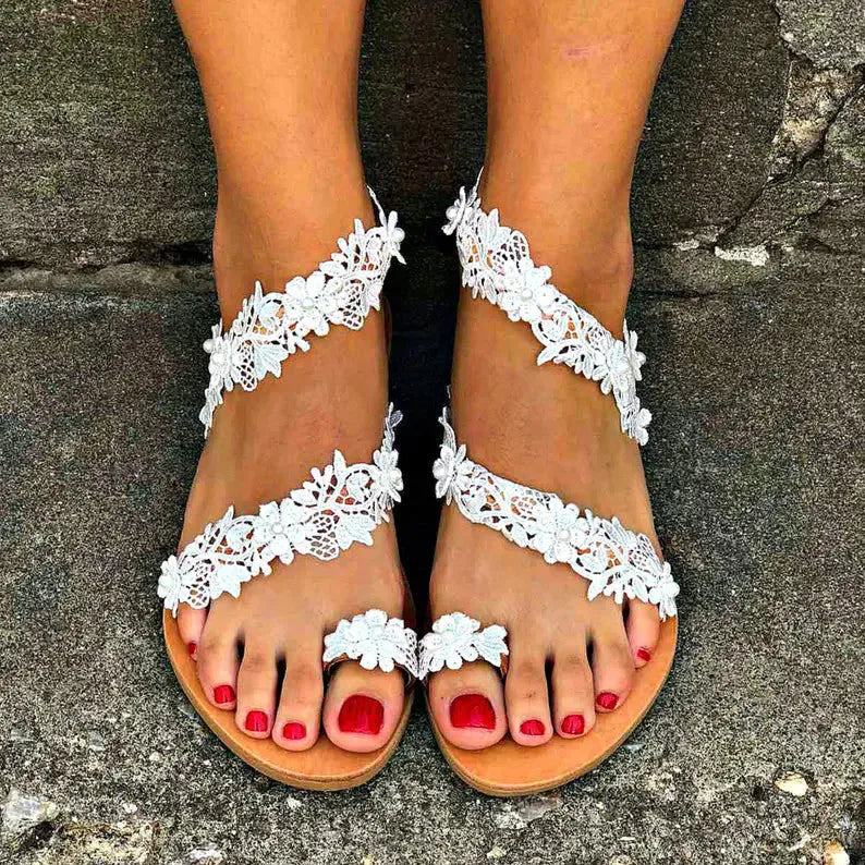 White flat sandals with rhinestone floral decoration on patent leather, showing backless slip-on design