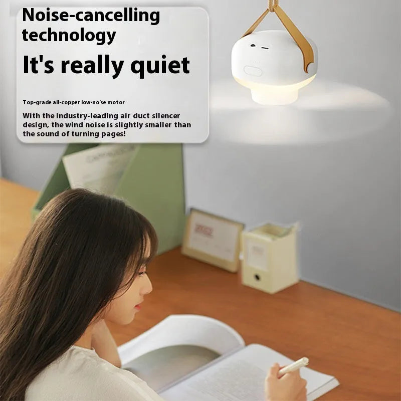 Small white rechargeable ceiling fan with fan blades and night light, hanging from a metal wire bracket for camping
