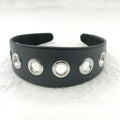 Wide black faux leather headband with round, square, and dotted rivets on a white background