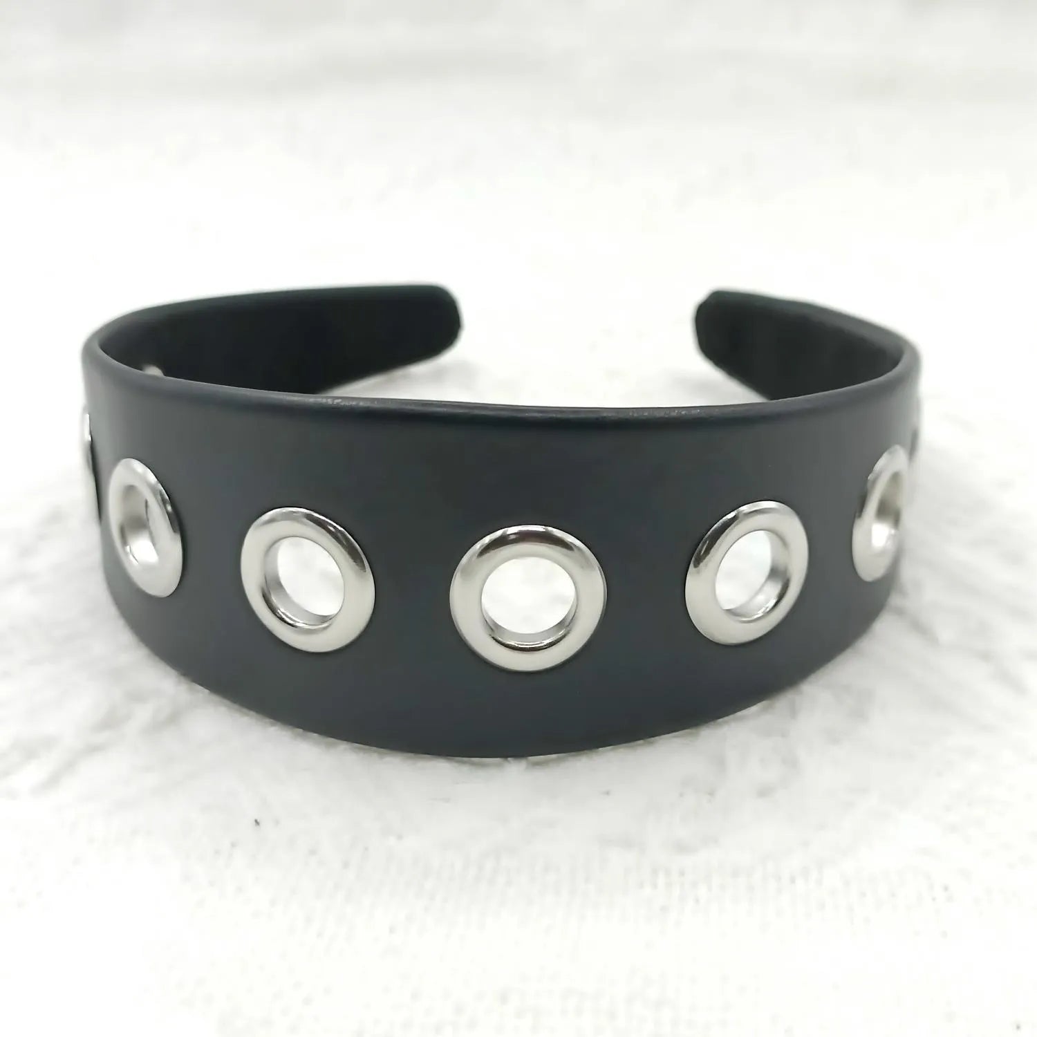 Wide black faux leather headband with round, square, and dotted rivets on a white background