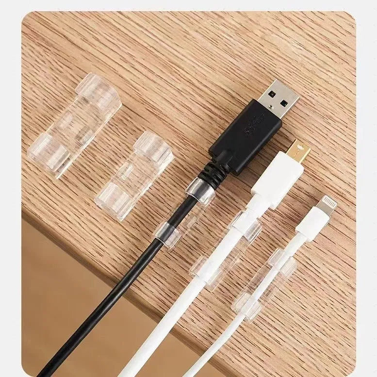 Transparent self-adhesive plastic wire holder snap clips for cable management on a white surface.