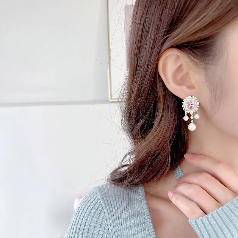 Oval-shaped copper drop earrings with inlaid zircon stones, white pearls, and a light purple tassel.