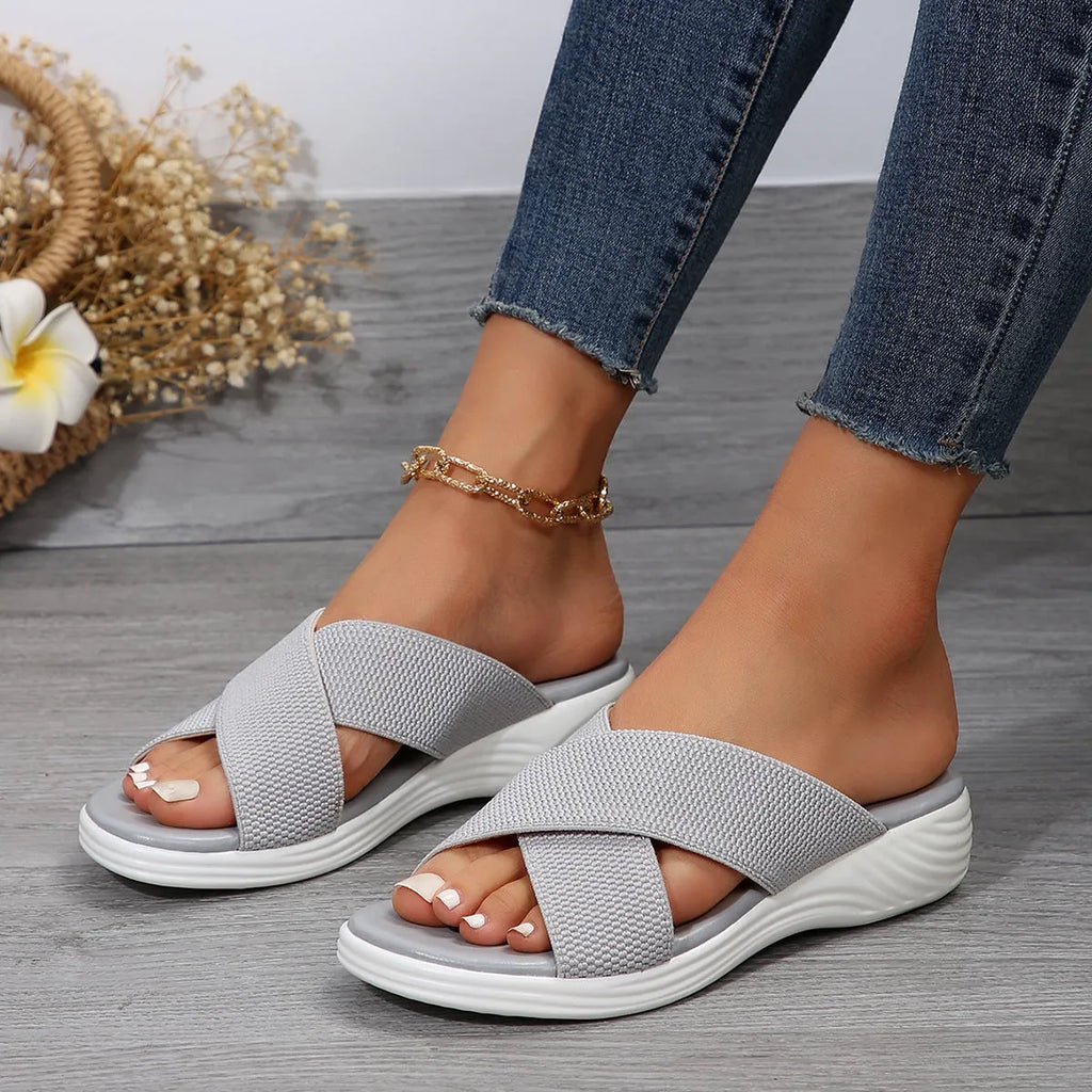 Women's black peep-toe wedge slippers with a cross strap and thick rubber sole on a grey background.