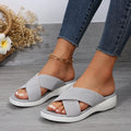 Women's black peep-toe wedge slippers with a cross strap and thick rubber sole on a grey background.