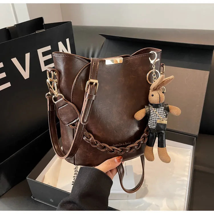 Women's retro PU messenger bag in brown with compact bucket shape, pendant, and double shoulder strap connector