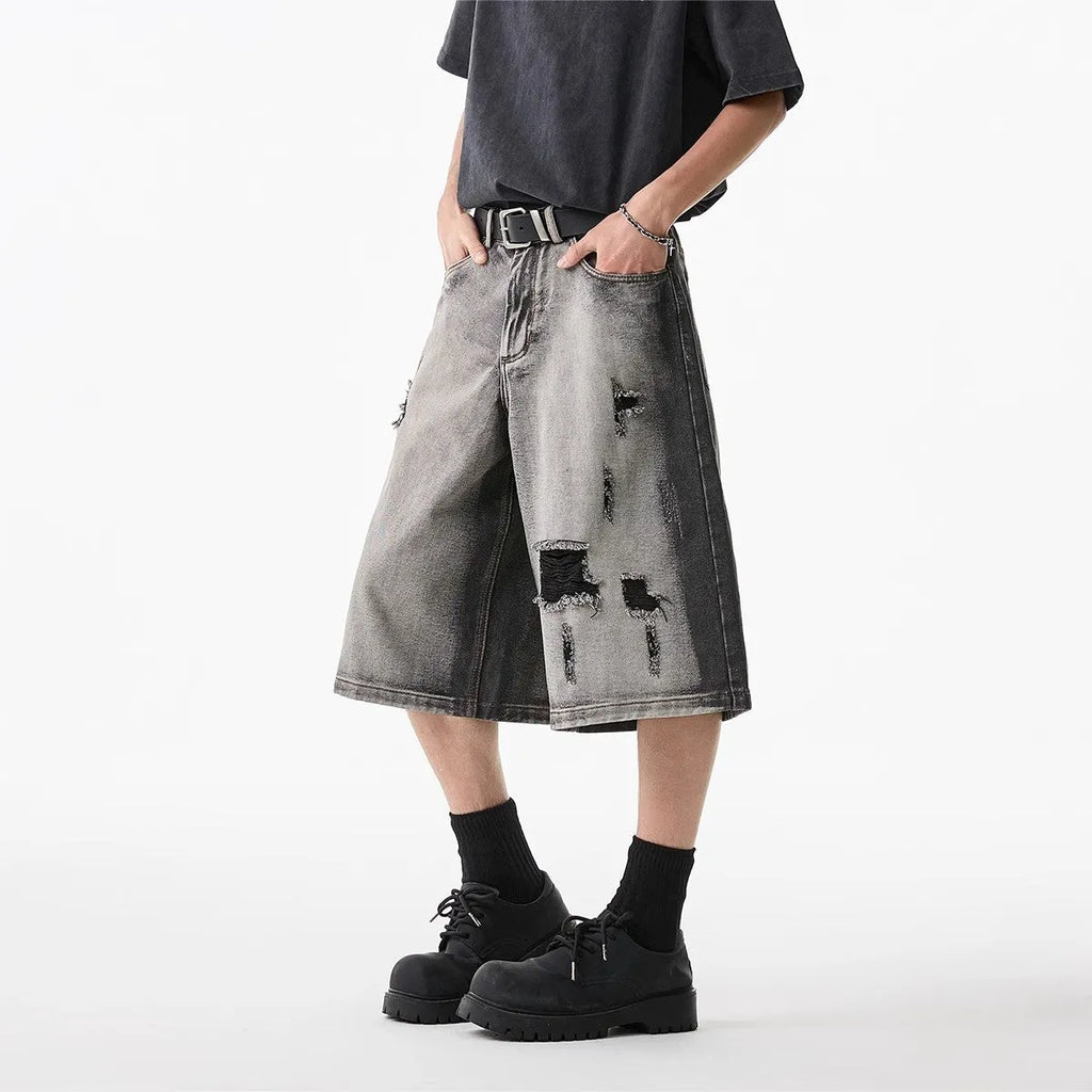 Grey distressed denim shorts with a loose cropped fit and hole details on a mannequin.
